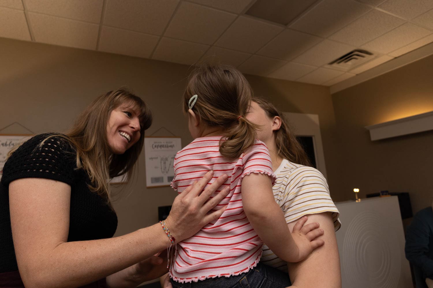 Dr. Tara helping a young girl, she is seen smiling and reassuring the girl before treatment while her mother holds the child